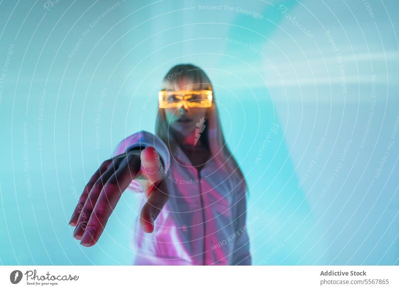 Frau mit leuchtender VR-Brille gestikuliert im Studio modern Schutzbrille Punkt Hand Erfahrung eintauchen selbstbewusst Piercing Virtuelle Realität