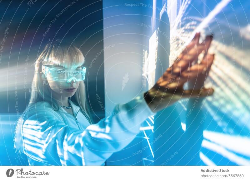 Frau in VR-Brille berührt Wand mit Lichtern berühren futuristisch erkunden Cyberspace Studioaufnahme sich[Dat] einbilden lange Haare Pony trendy Stil blond