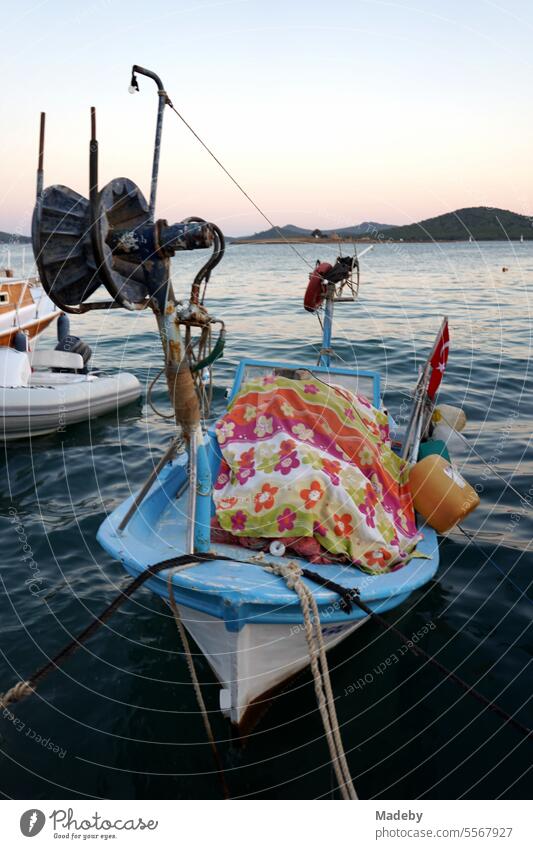Romantische Abendstimmung am Meer mit Fischerboot und Umlenkrolle im Licht der Abendsonne mit Pier am Hafen in der Bucht von Ayvalik am Ägäischen Meer in der Provinz Balikesir in der Türkei