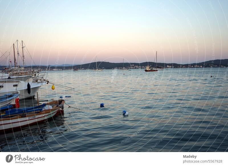 Romantische Abendstimmung am Meer mit Booten und Yachten im Licht der Abendsonne mit Leuchtturm und Pier am Hafen in der Bucht von Ayvalik am Ägäischen Meer in der Provinz Balikesir in der Türkei