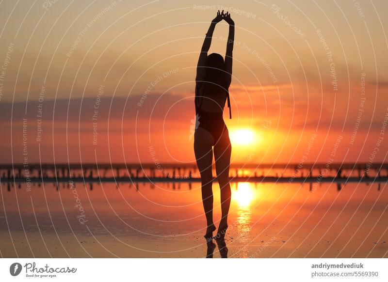 Silhouette einer jungen schlanken Frau im Badeanzug, die bei Sonnenuntergang am Meer tanzt. MEER Himmel Sonnenaufgang Strand Menschen Sommer Wasser Mädchen