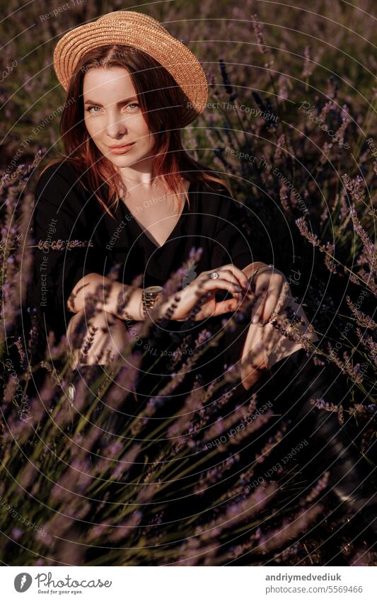 Junge romantische Frau in schwarzem Kleid und Strohhut sitzt in blühenden duftenden lila Lavendelfeld. Attraktives brünettes Mädchen genießt das Leben und träumt. Natürliche Schönheit Konzept