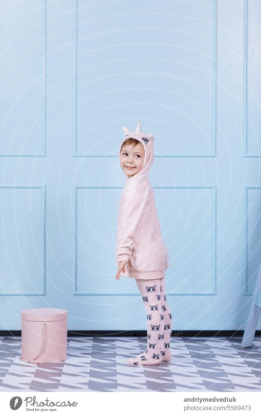 Lächelnde schöne kleine Mädchen in Einhorn rosa Kostüm ist lächelnd und Spaß auf einer blauen Wand Hintergrund. glückliche Kindheit. wenig Hut Gesicht niedlich