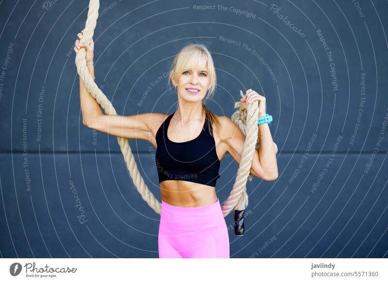 Fitte Frau mit Gymnastikseil im Fitnessstudio Seil selbstbewusst Aufsteiger Training Übung passen Aktivität Sportkleidung Wellness aktiv blond Athlet Gesundheit