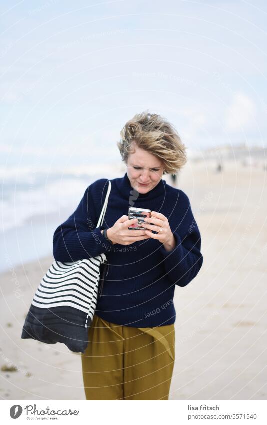 UND NUN? Frau 30 bis 40 Jahre Strand Meer Ferien & Urlaub & Reisen Handy Handy halten daddeln Farbfoto Erwachsene Außenaufnahme windig Junge Frau Erholung