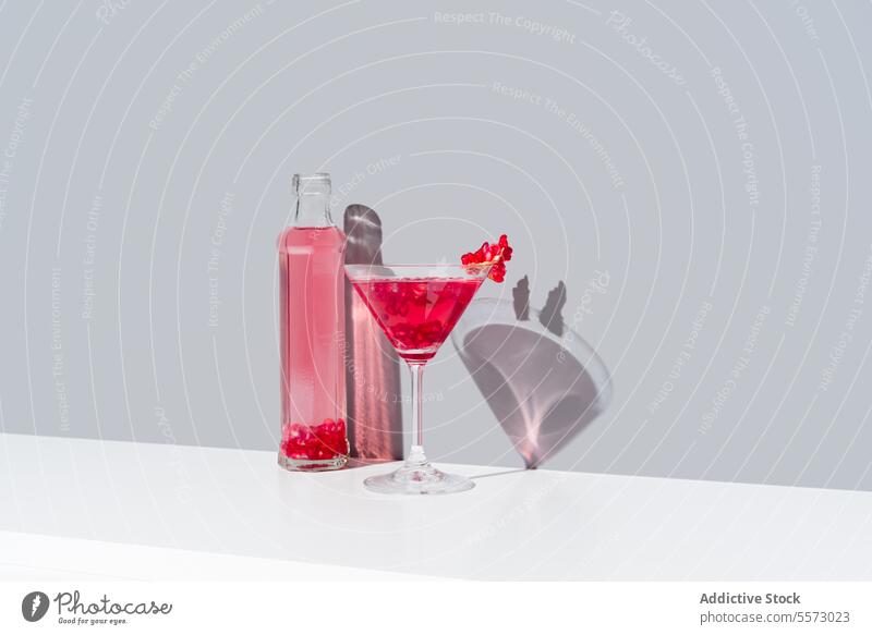 Granatapfel-Cocktail und Flaschen-Duo auf grauem Hintergrund Glas rot Garnierung Schatten pulsierend Getränk trinken Präsentation elegant dekorativ Belag
