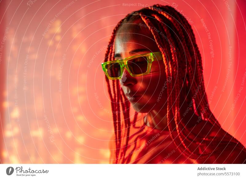 Frau mit orangefarbenen Zöpfen steht in Neonlicht jung Porträt Metaversum neonfarbig Afro-Zöpfe abstrakt ernst selbstbewusst Individualität Vorschein