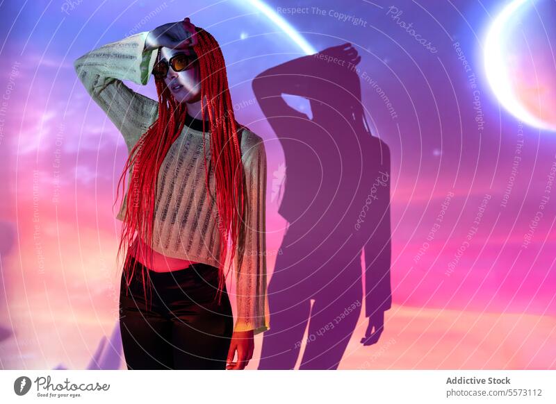 Frau mit orangefarbenen Zöpfen steht in Neonlicht jung Porträt Metaversum neonfarbig Afro-Zöpfe abstrakt Projektor virtuell futuristisch Vorschein erweitert