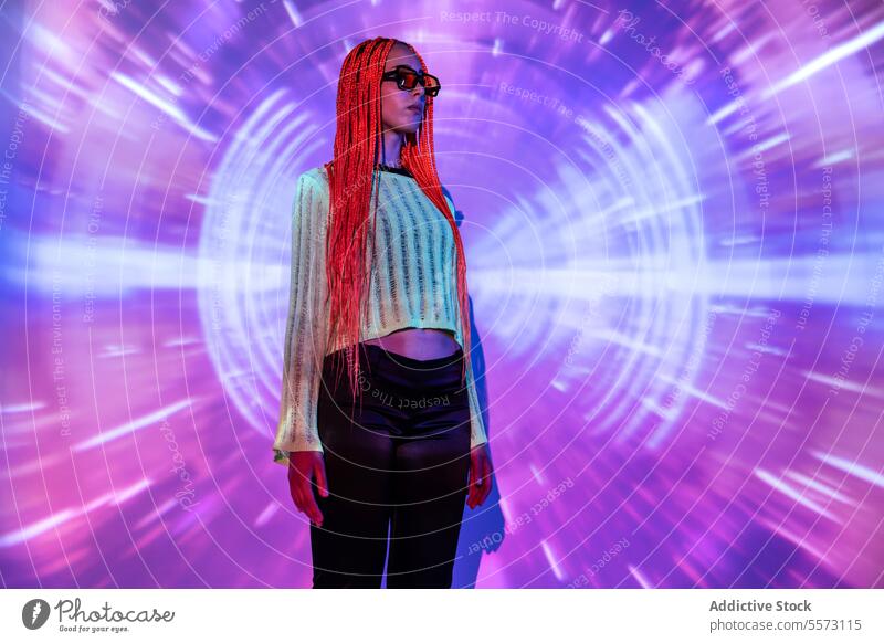 Frau mit orangefarbenen Zöpfen steht in Neonlicht jung Porträt Metaversum neonfarbig Afro-Zöpfe abstrakt Projektor Individualität virtuell futuristisch