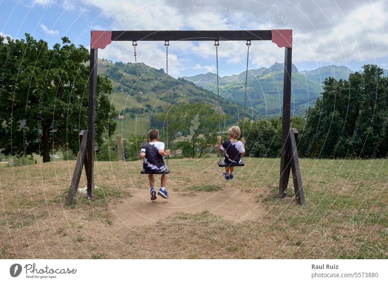 Zwei Kinder schwingen sich auf dem Rücken dem Berg entgegen Aktion Genuss Aufregung Unschuld Freude Kindergarten Lachen spielen spielerisch Spielen Vorschule