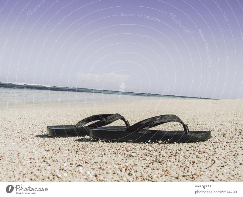 Flip-Flops am Strand vor dem Meer. Blauer Himmel im Hintergrund. schwarz Zehentreter Sommer Erholung Ferien Urlaub Reisen Tourismus Sandale baden schwimmen Mode