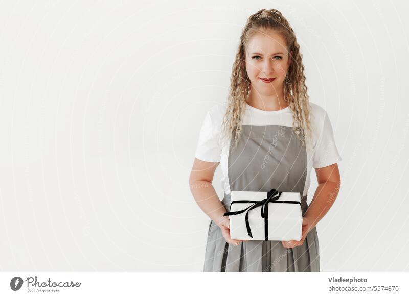 Junge Frau in Schürze hält weiße Geschenkbox mit Geschenkbandschleife in der Hand. Schwarz weiß Kasten präsentieren Geburtstag Überraschung Feiertag Beteiligung