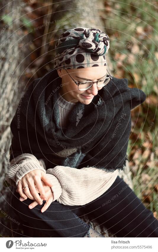 BAUMSTAMM - SITZENDE FRAU - WARTEN Frau 18-30 Jahre Kopftuch Brille Herbst Schal Baumstamm laub bunte Blätter Natur Erwachsene Farbfoto Außenaufnahme