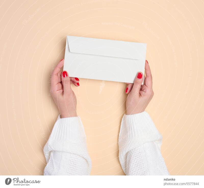 Zwei weibliche Hände halten einen weißen rechteckigen Umschlag auf beigem Hintergrund, Ansicht von oben Brief Post Nachricht Papier Beitrag senden zeigend