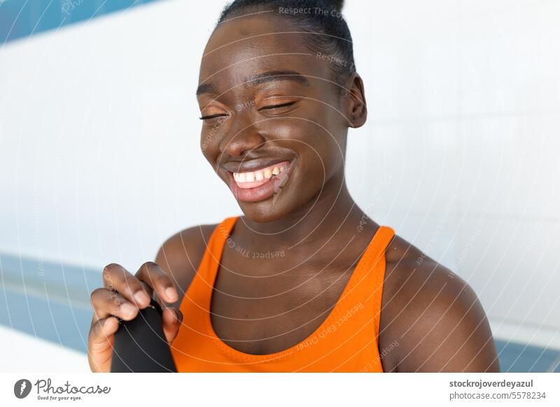 Schwarze junge Frau lächelt und hält ihre Wasserflasche in der Hand, während sie auf einer Bank im beheizten Schwimmbad sitzt schwarz Afrikanisch Person Glück