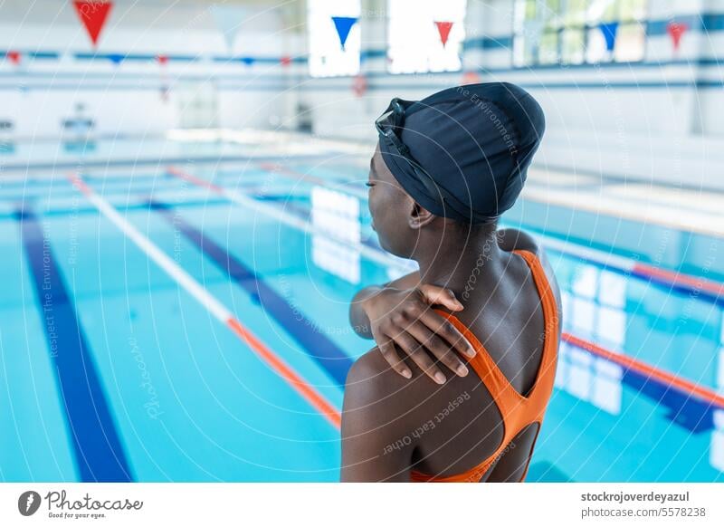 Schwarze junge Frau, die ihre schmerzende Schulter im Schwimmbad berührt Wasser Sport Schmerz Verletzung schwarz erhitzt Badeanzug orange Lächeln blau Lifestyle