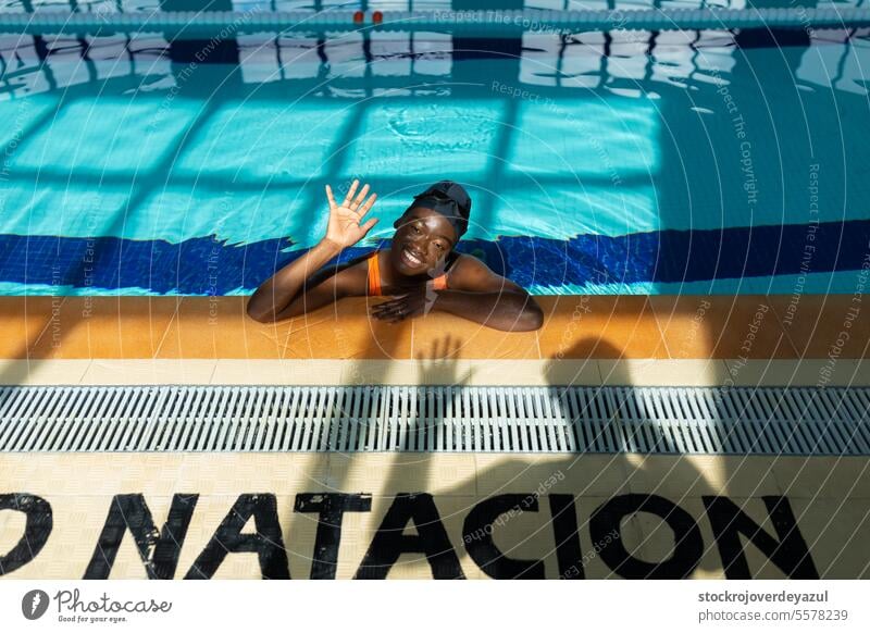 Schwarze junge Frau winkt entspannt am Straßenrand während eines Bades im Schwimmbad Pool Wasser Person Sport Schwimmer aktiv schwarz erhitzt Badeanzug orange