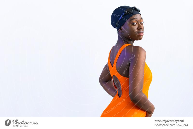 Schwarze junge Frau im Badeanzug, die in die Kamera schaut und vor einem schlichten weißen Hintergrund posiert schwarz Schwimmbad erhitzt orange Gesundheit