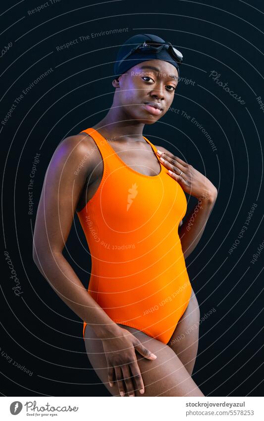 Schwarze junge Frau im Badeanzug, die vor einem schlichten schwarzen Hintergrund posiert Person Frauen Schwimmbad erhitzt orange Gesundheit Lächeln Lifestyle
