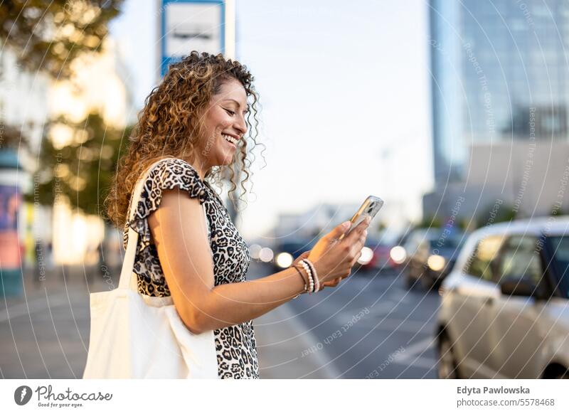 Junge Frau bucht ein Taxi über eine mobile App auf der Straße in der Stadt junger Erwachsener außerhalb Selbstvertrauen Lächeln genießen Lachen Freude Spaß