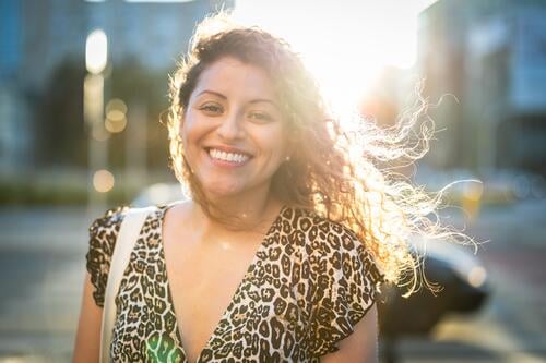Porträt einer lächelnden jungen Frau mit lockigem Haar in der Stadt junger Erwachsener Straße außerhalb Selbstvertrauen Lächeln genießen Lachen Freude Spaß