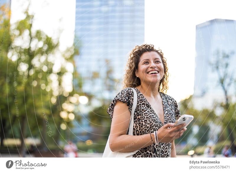 Porträt einer lächelnden jungen Frau, die in der Stadt ein Mobiltelefon benutzt junger Erwachsener Straße außerhalb Selbstvertrauen Lächeln genießen Lachen