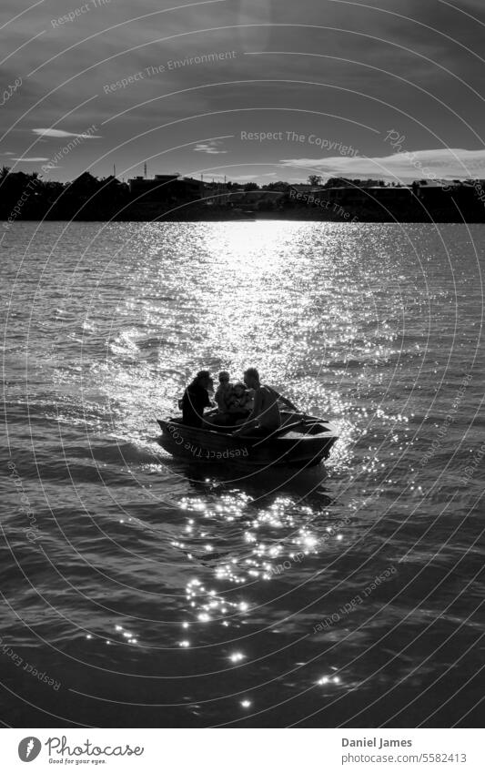 Drei Personen in einem kleinen Boot, das von einer hellen Sonne beschienen wird. Wasser Hafen Schwarzweißfoto Silhouette Wasserfahrzeug Meer Außenaufnahme
