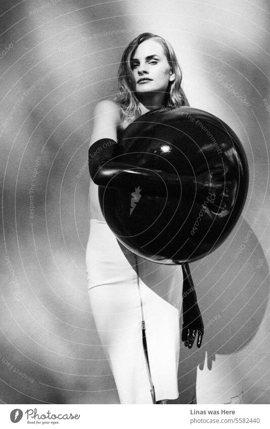 Ein umwerfendes brünettes Model posiert anmutig mit einem großen schwarzen Luftballon und trägt ein elegantes Latex-Outfit. Inklusive langer schwarzer Handschuhe. Die Frau mit dem hübschen Gesicht macht bei diesem Modeltest eine hervorragende Figur.