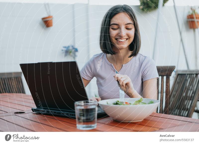 Junge Freiberuflerin arbeitet am Laptop und isst Salat, gesunde Menschen, arbeiten zu Hause Konzept. Tablette Ergänzung Frau Glück Schmerztablette Vitamin