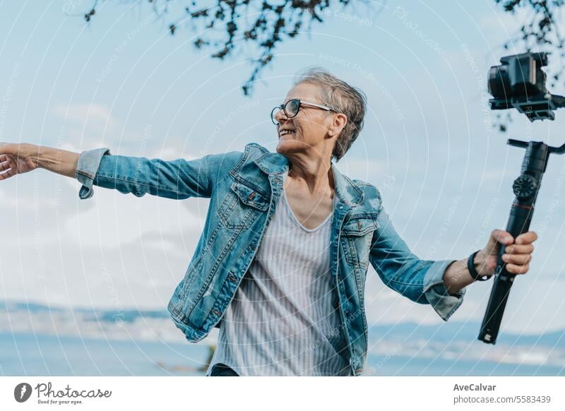 Eine lächelnde Rentnerin, die in der Nähe des Meeres einen Live-Stream macht, Followern antwortet und Hallo sagt. Frau Ruhestand Luftschlange live Video