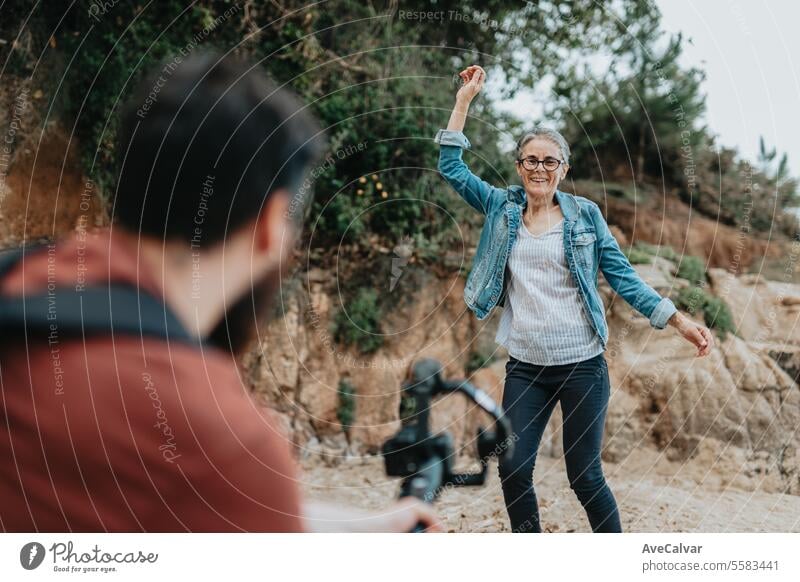 Der Sohn hilft seiner Mutter, ein Video vom Tanzen am Strand aufzunehmen und folgt damit den Trends in den sozialen Medien. Senior Frau Luftschlange live