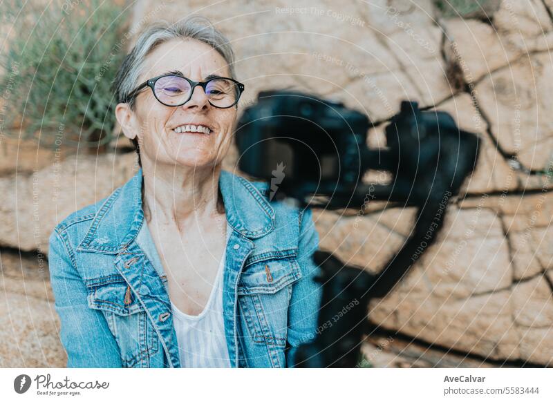 Eine lächelnde Rentnerin, die in der Nähe des Meeres einen Live-Stream macht, Followern antwortet und Hallo sagt. Ruhestand Person Frau Luftschlange live Video