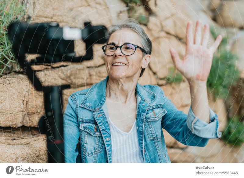Eine lächelnde Rentnerin, die in der Nähe des Meeres einen Live-Stream macht, Followern antwortet und Hallo sagt. Frau Erwachsener Person Luftschlange live