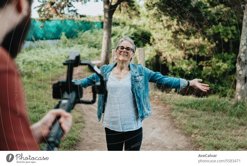 Eine ältere, jubelnde Frau erklärt ihren Followern ihre Reise, während ein Mann sie live in den sozialen Medien aufnimmt. Senior Luftschlange Video Ruhestand