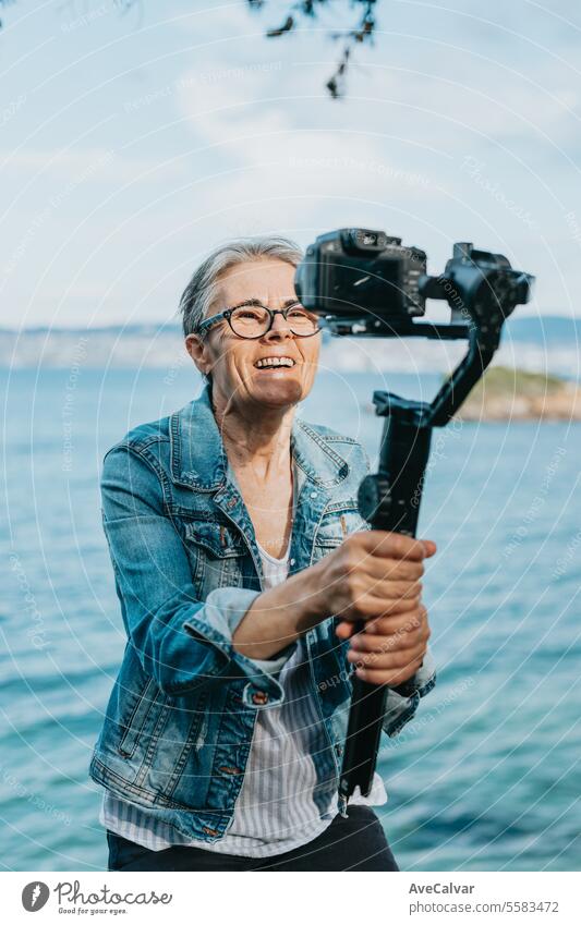 Ältere fröhliche Frau, die ein Video für ihre Familie aufnimmt, in dem sie ihren Urlaub erklärt. Alter Fotograf. Luftschlange live Ruhestand Person Erwachsener
