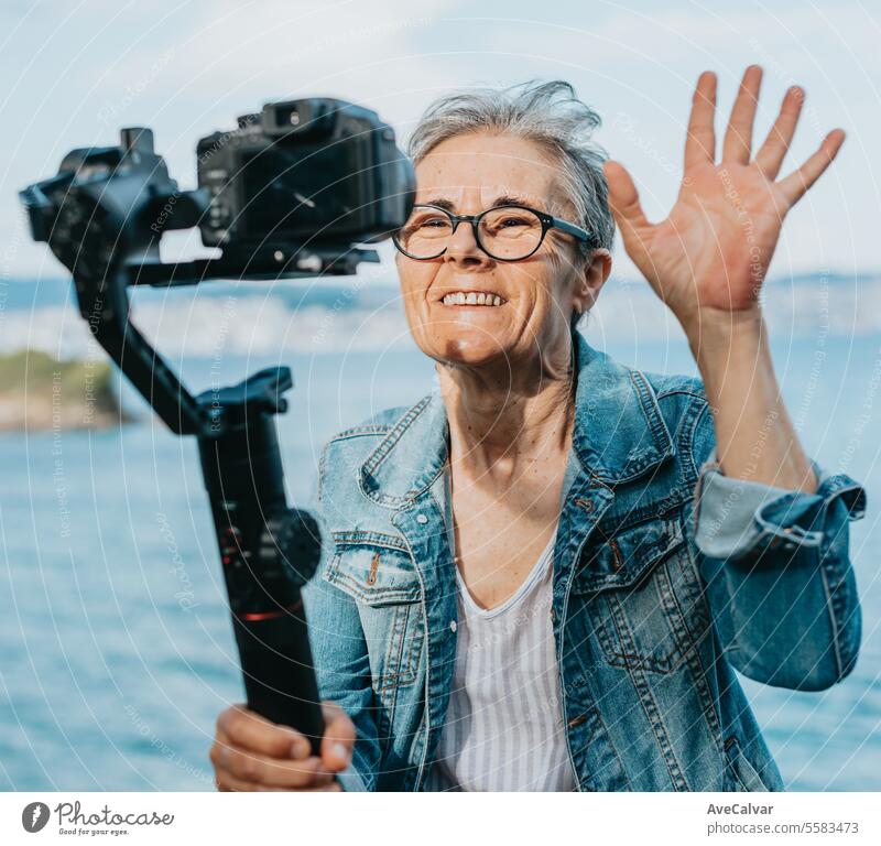 Eine lächelnde Rentnerin, die in der Nähe des Meeres einen Live-Stream macht, Followern antwortet und Hallo sagt. Luftschlange live Video Ruhestand Frau