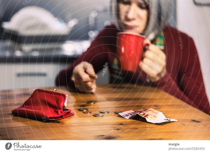 Eine traurige Frau in der Küche zählt ihr Haushaltsgeld Geld zählen Geldmünzen Geldscheine Bargeld Hand Armut Tasse Euro sparen Geldbörse rot Tisch