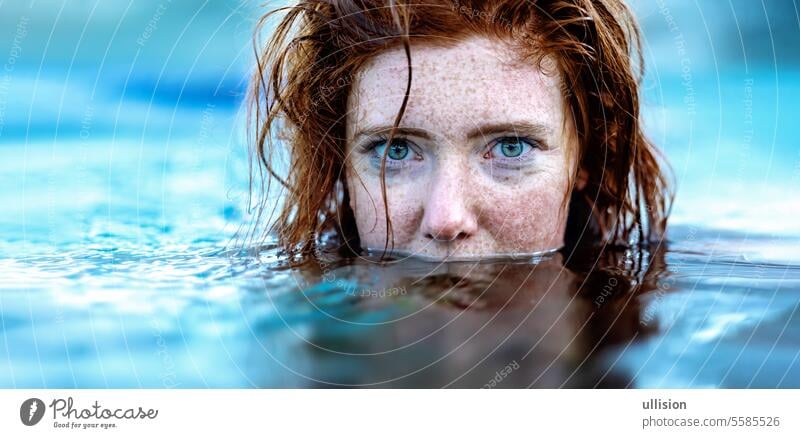 Porträt einer sexy, jungen rothaarigen Frau mit Sommersprossen und rotem, nassem Haar, im türkisfarbenen Spa-Poolwasser, Kopf halb unter Wasser Rotschopf