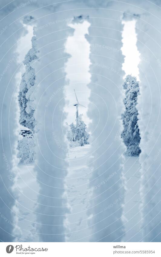 Blick durch einen verschneiten Zaun auf eine Winterlandschaft mit Windrad winterlich Schnee Frost schneebedeckt Wintertag Winterstimmung Schneedecke Kälte