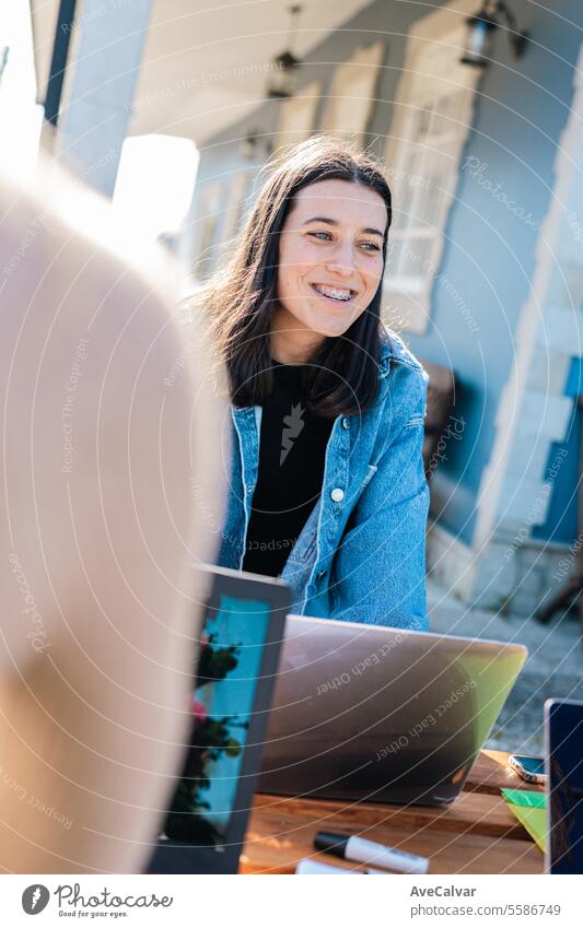 Junge, fröhliche Frau, die am Laptop arbeitet und sich mit ihren Kollegen in einer Pause auf einer Terrasse im Freien unterhält. Menschengruppe Schüler Freunde