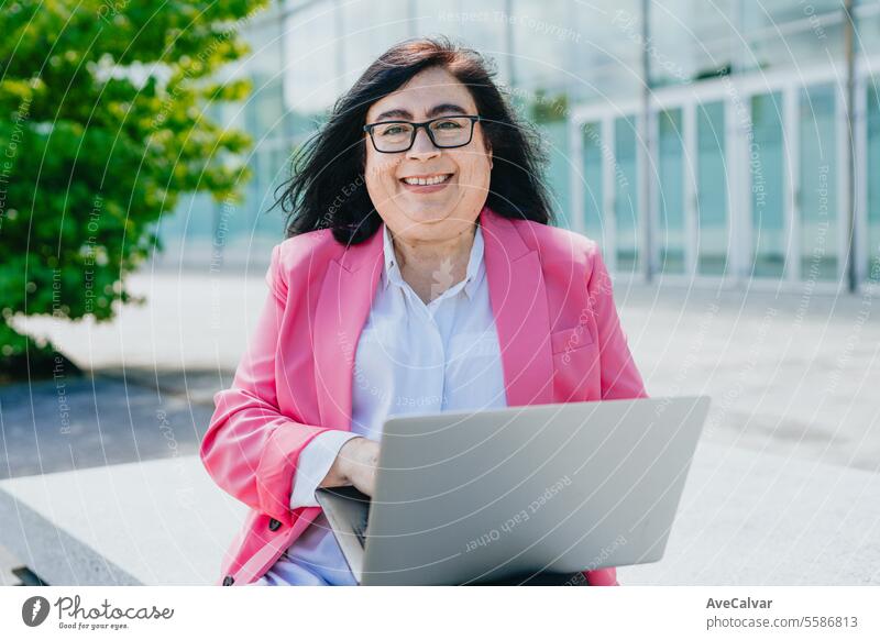 Fröhliche erwachsene Geschäftsfrau, die einen Laptop auf dem Schoß hält, lächelt und die frische Luft genießt. Erwachsener Business Frauen Person Computer
