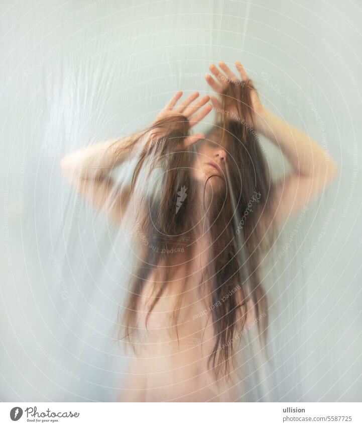 verschwommenes, unscharfes Bild einer sinnlichen, romantischen, nackten, sexy Frau, die hinter einer Plastikfolie mit ihren Haaren spielt und sich in Ekstase bewegt