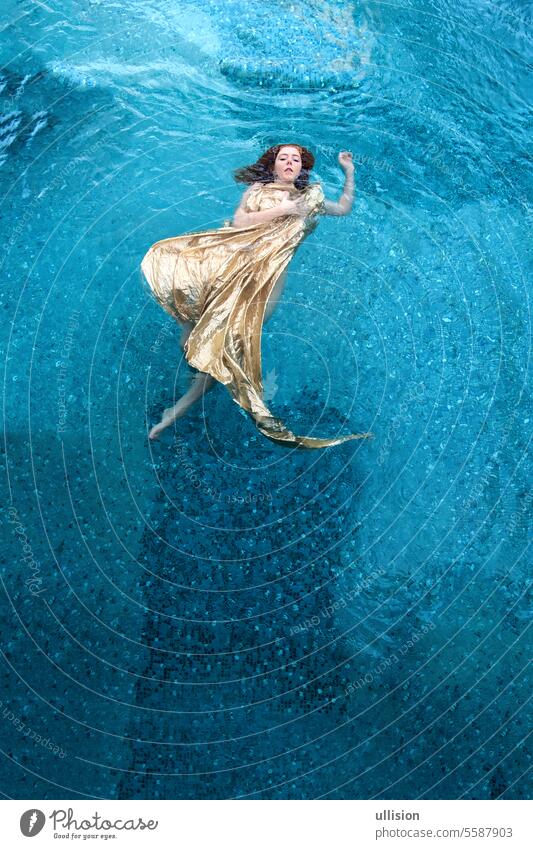 Draufsicht auf schöne junge sexy rothaarige Frau in goldenem Kleid, Abendkleid, schwebt schwerelos elegant im türkisfarbenen Wasser im Pool Top Ansicht