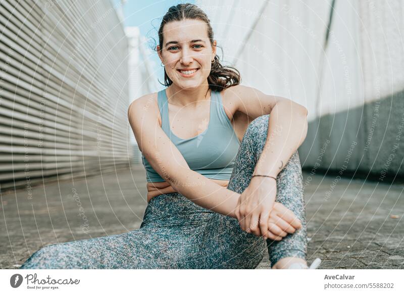 Eine fitte, lächelnde und fröhliche junge Frau in Sportkleidung sitzt auf dem Boden in einer städtischen Straßenszene. Person Schönheit Erwachsener Lifestyle
