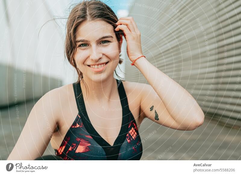 Porträt eines jungen Mädchens in Sportkleidung, das in einer städtischen Umgebung in die Kamera lächelt und ihr Haar berührt. Frau Person Erwachsener Schönheit