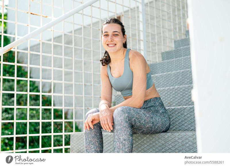 Porträt eines lächelnden und fröhlichen jungen Mädchens in Sportkleidung, das auf einer Treppe sitzt. Sport in der Stadt. Frau Frauen Lifestyle Gesundheit