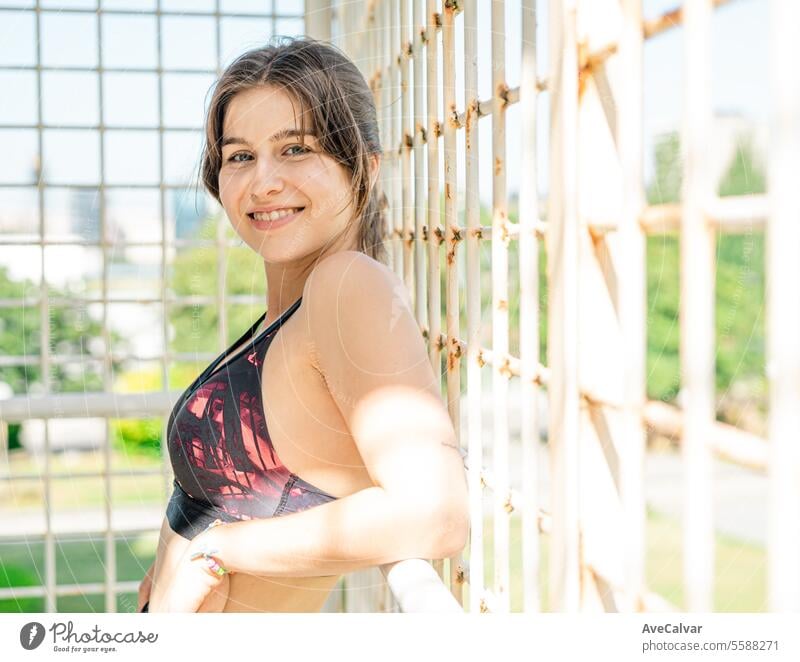 Sportliche und gesunde junge lächelnde Frau, die sich an einen weißen Zaun in einer städtischen Umgebung lehnt. Frauen Person Sommer Schönheit hübsch Lifestyle