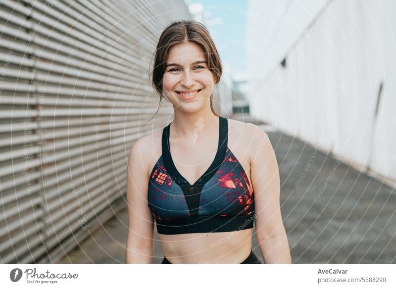 Porträt eines lächelnden weiblichen Fitnesstrainers, der in einer städtischen Straßenumgebung in die Kamera schaut. Frauen Sport Schönheit jung passen Übung