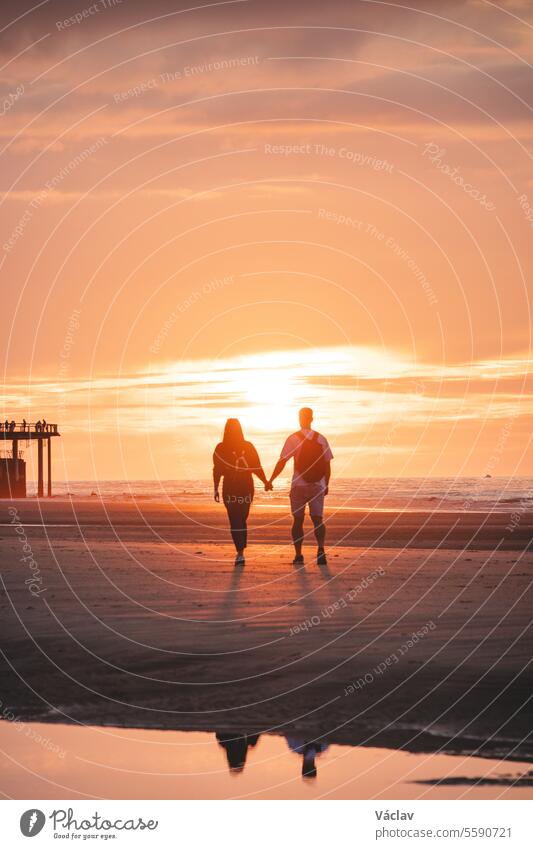 Romantischer Spaziergang eines jungen Paares an den Stränden von Oostende in Westbelgien bei Sonnenuntergang. Liebe und Hingabe. Spiegelung in einem Wasserbecken