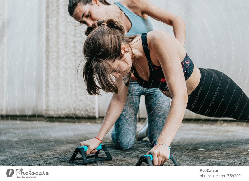 Zwei junge Mädchen helfen sich gegenseitig bei Liegestützen, wobei sie auf ihre Körperhaltung achten, um ihre Muskeln zu stärken. Sport Training Frauen
